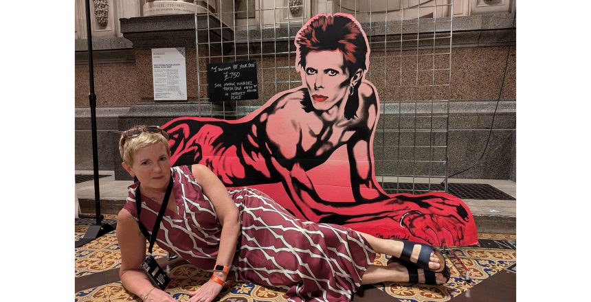 Woman with short fair hair lying down in front of a half man/ half dog cutout
