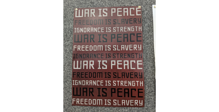 Red poster with black and white lettering with the words: War is Peace, Freedom is Slavery, Ignorance is Strength